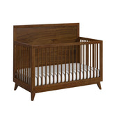 Malia crib in walnut with high wood-grain headboard, spindle rails and tapered feet, angled view