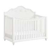 Alana crib in white, angled view showing curved front rail, carved bow headboard and bun feet